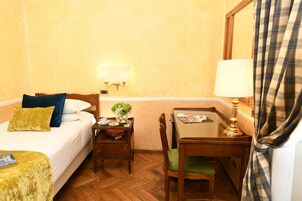 A hotel room with a bed, a desk, a chair, and a table.