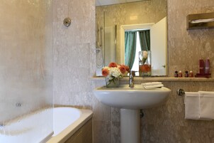 Une salle de bain avec une baignoire, un lavabo agrémenté d’un vase de fleurs, une douche et un miroir.