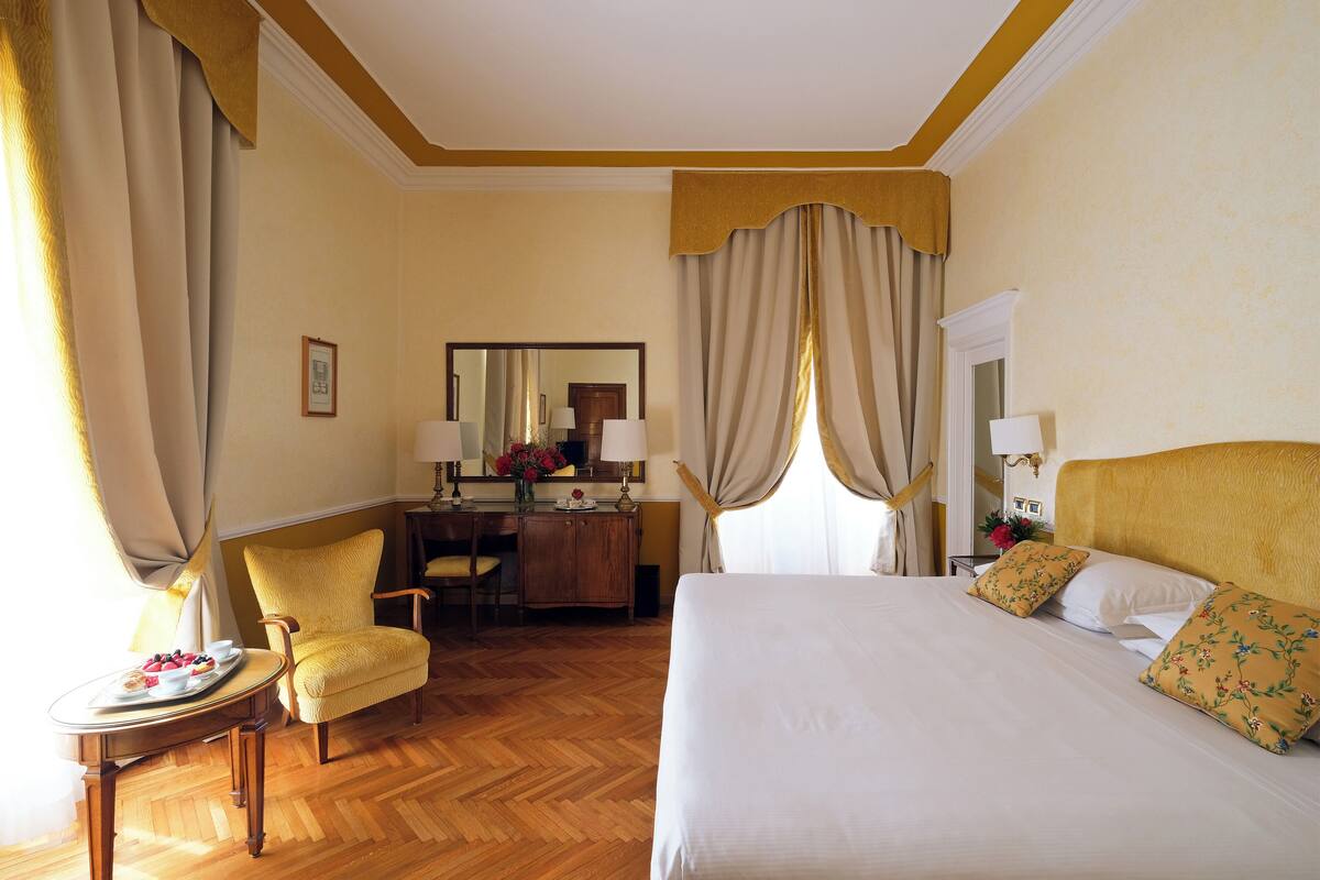 Ein Hotelzimmer mit einem großen Bett, einem Schreibtisch, einem Stuhl und einem kleinen Tisch mit einer Obstschale.