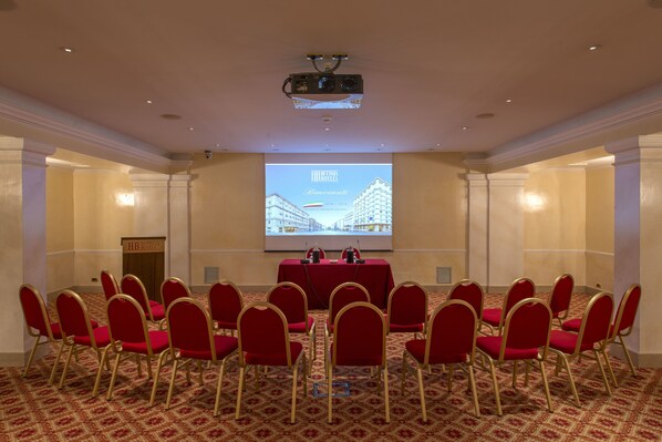 A conference room with a large screen displaying a presentation, red chairs arranged in a semi-circle, and a podium at the front. - Bettoja Hotel Massimo D'Azeglio (Rome)
