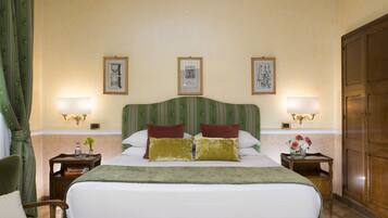 Una camera d'albergo con un letto grande, due lampade ai lati del letto, quadri appesi al muro, una testiera a righe verdi e un armadio in legno.