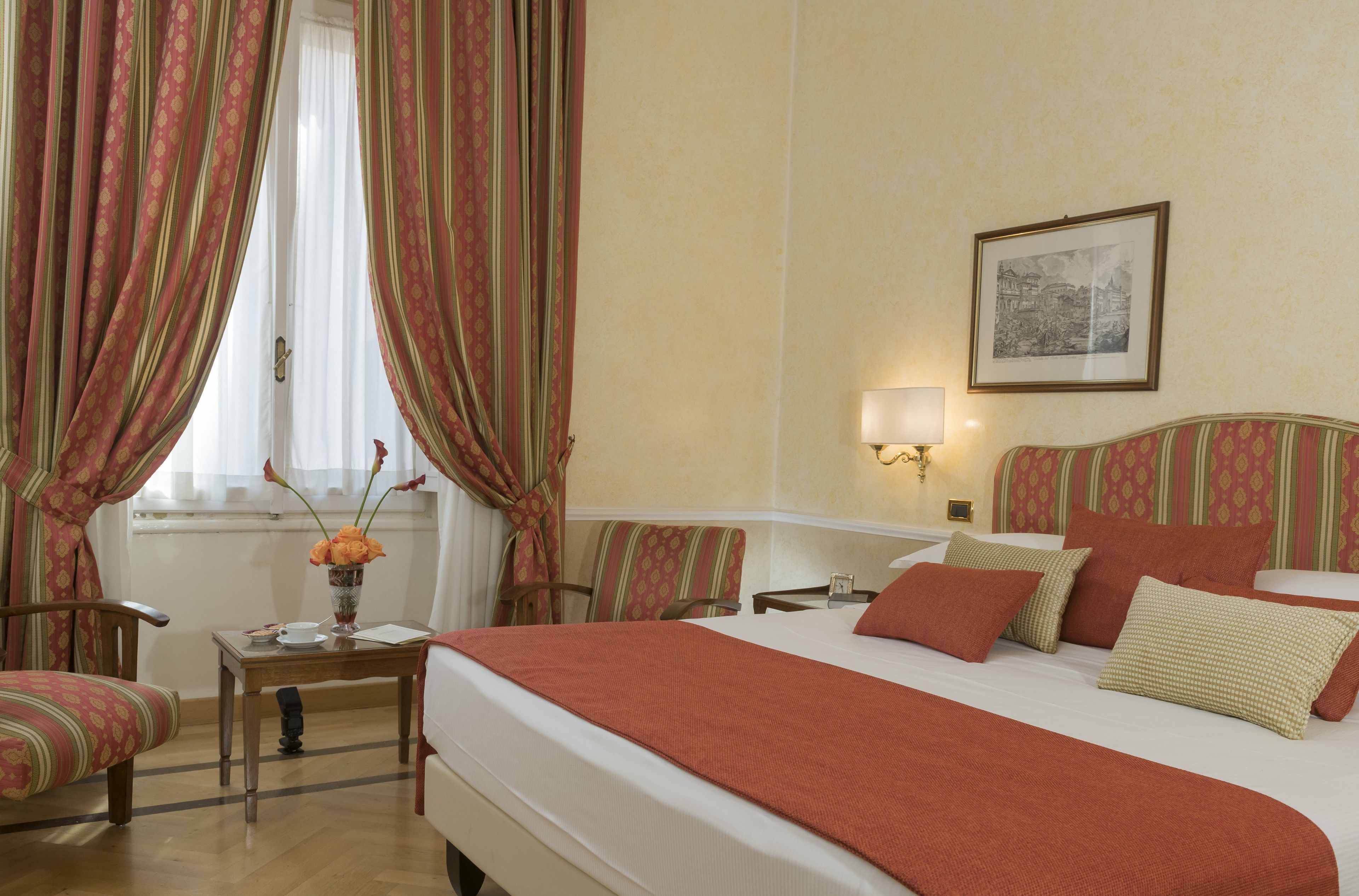 A hotel room with a bed, a chair, a table, and a lamp.