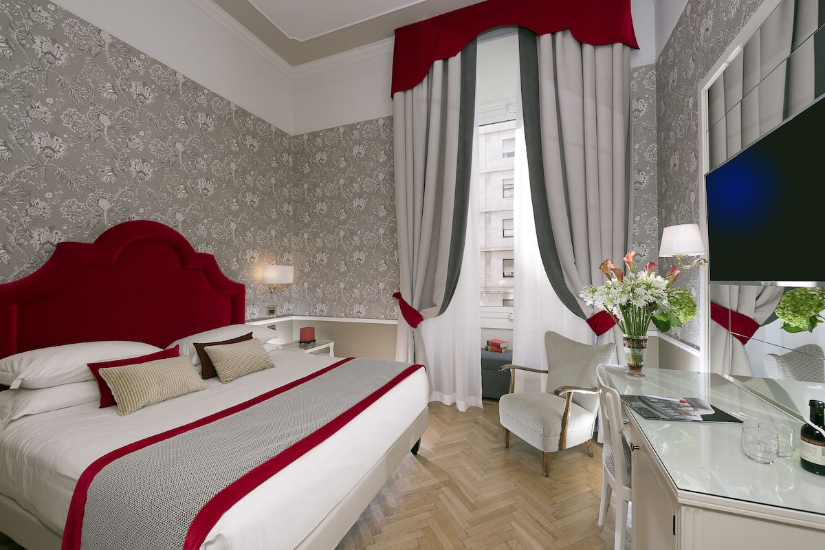 Ein Hotelzimmer mit einem großen Bett, einem Schreibtisch mit Stuhl, einem Fernseher und einem Fenster mit Vorhängen.