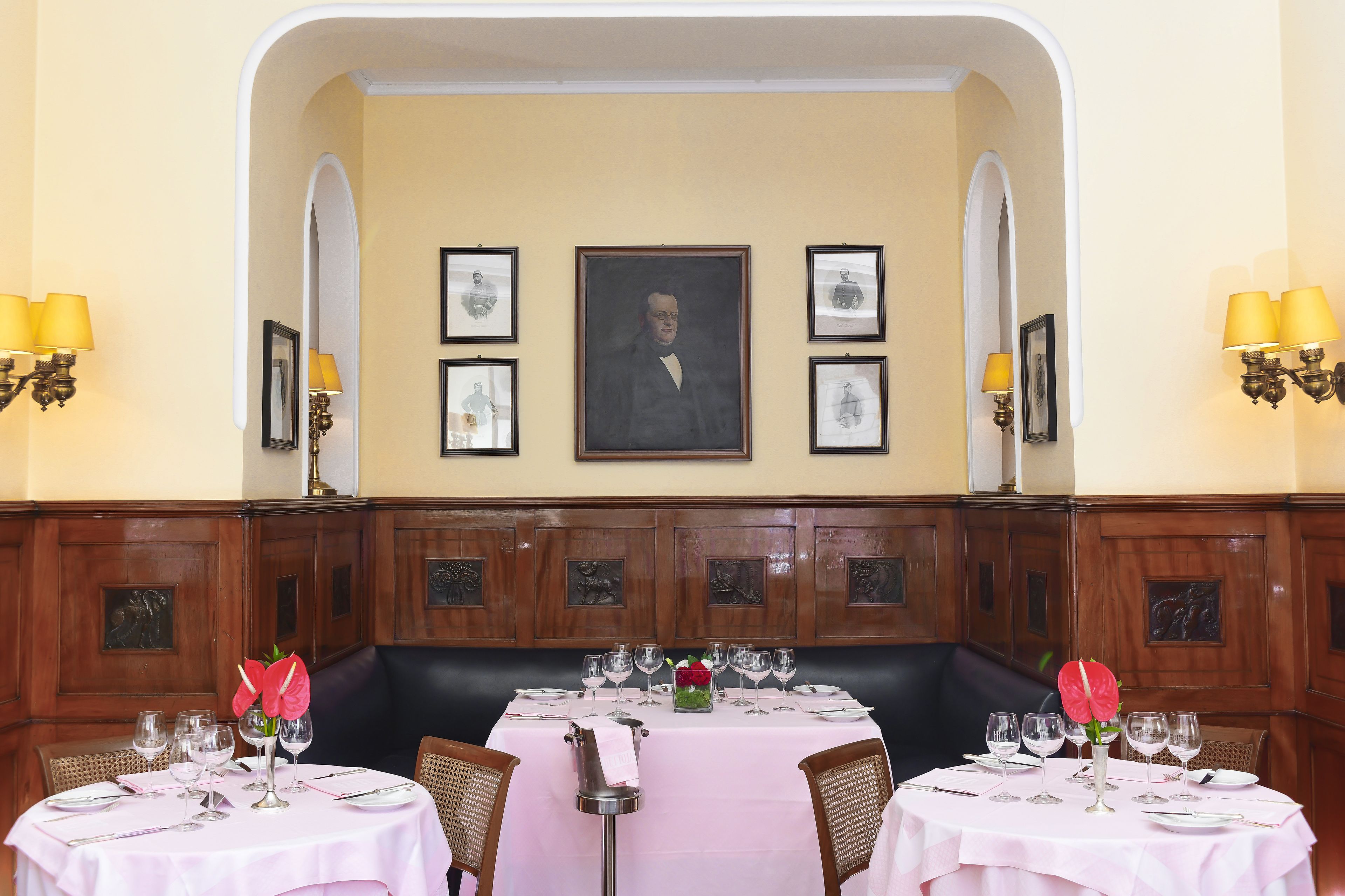 A dining area with a table set for two, a portrait above the table, and wooden paneling on the walls.