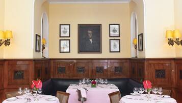 A dining area with a table set for two, a portrait above the table, and wooden paneling on the walls.