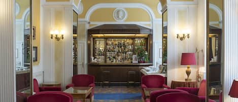 Un hall d’hôtel avec des fauteuils rouges, un coin bar et une moquette à motifs.