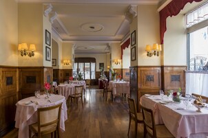 A dining area with round tables, wooden chairs, and chandeliers.