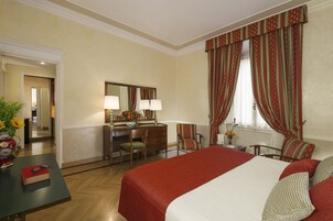 A hotel room with a large bed, a desk with a chair, a dresser, and a mirror.