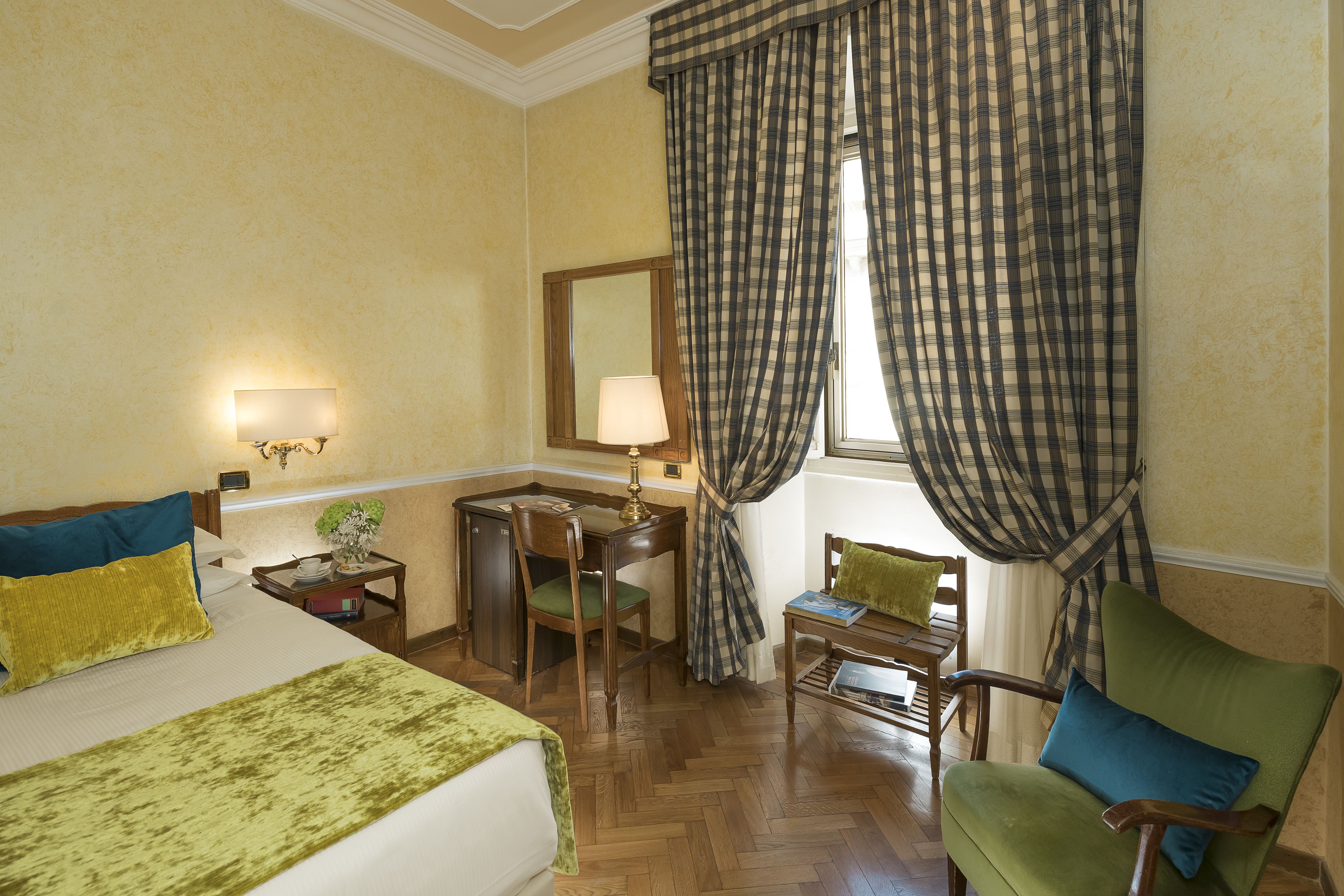 Une chambre d’hôtel avec un lit, un bureau, une chaise et une fenêtre avec des rideaux.