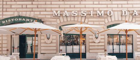 An outdoor seating area with tables and umbrellas in front of a building with the sign "MASSIMO DA RISTORANTE".