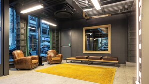 A modern lobby with leather chairs, a yellow rug, and a large mirror reflecting the interior. - Smart Hotel Milano (Milan)