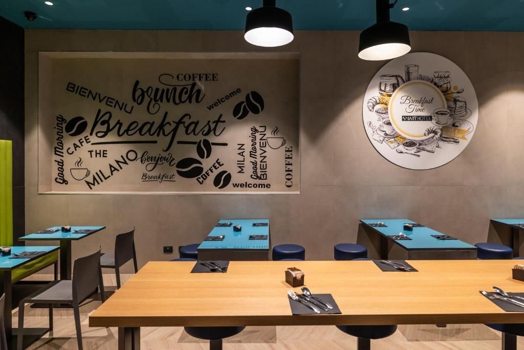 Uma zona de pequeno-almoço moderna com mesas, cadeiras e uma parede com palavras e ilustrações sobre café.