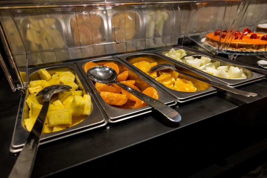A buffet with various food items including pineapple, orange slices, and white cubes, likely cheese or yogurt.