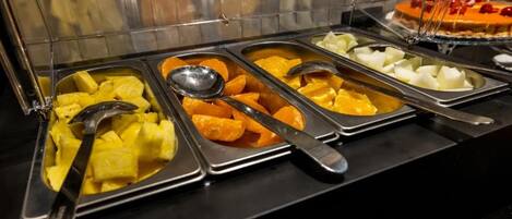 A buffet with various food items including pineapple, orange slices, and white cubes, likely cheese or yogurt.