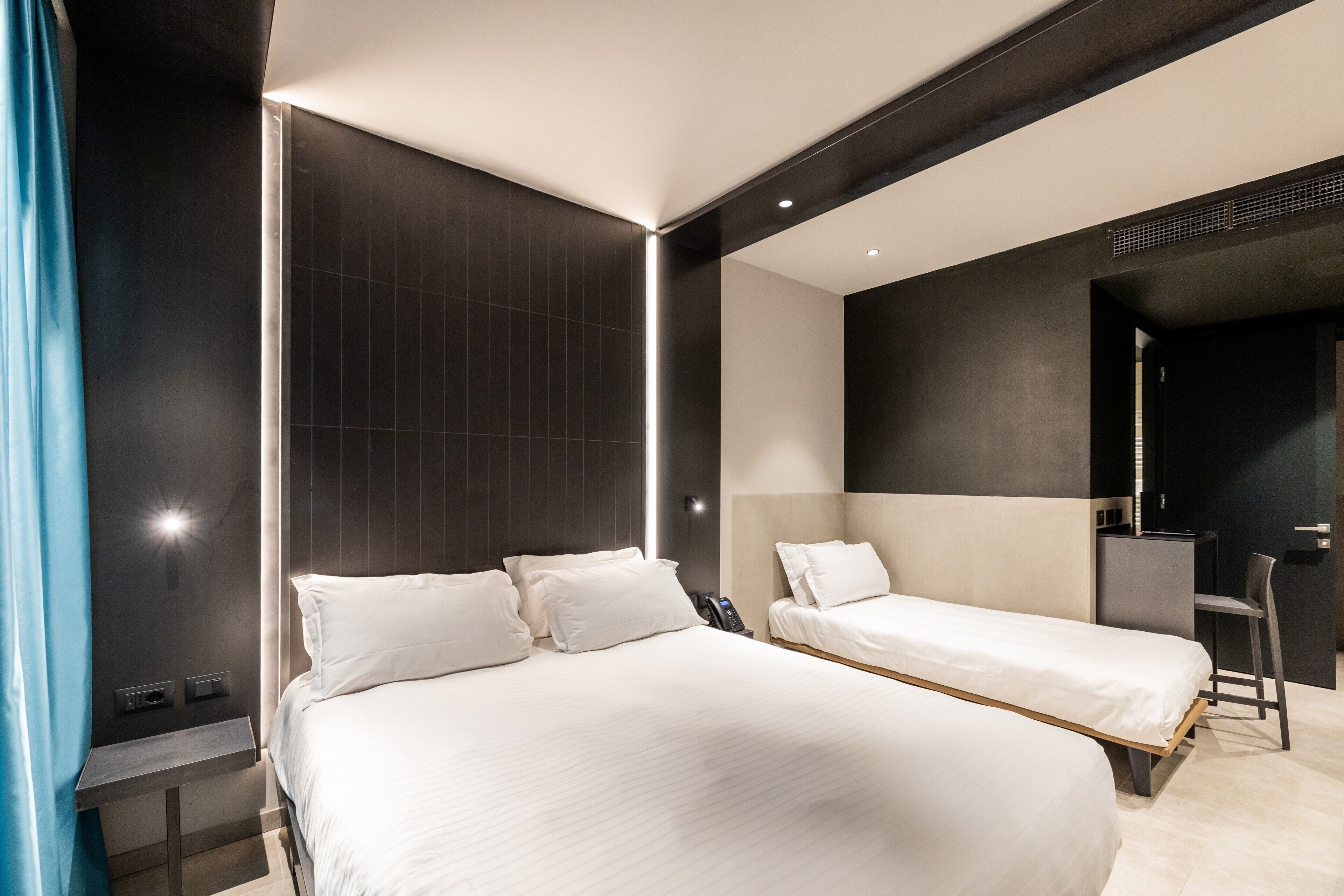 A modern hotel room with two beds, a desk, and a chair.