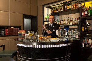Un'area bar con un barista, diverse bottiglie di liquori e un bancone ben fornito.