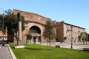 Een historisch gebouw met een grote bogenpoort, een standbeeld op de voorgrond en een verzorgd gazon.
