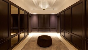 A hallway with dark wood paneling, a round ottoman, and a chandelier. - Mascagni Hotel (Rome)