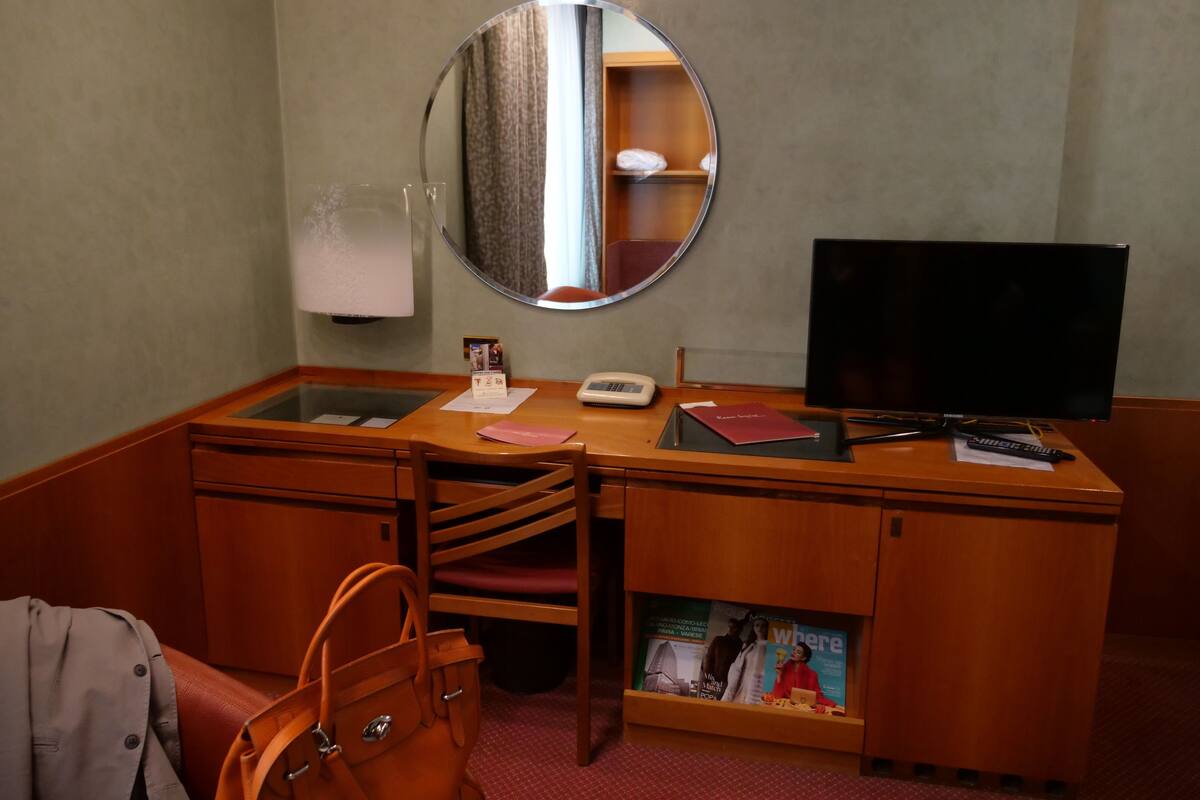 Una habitación de hotel con un escritorio de madera, televisor, teléfono y espejo.