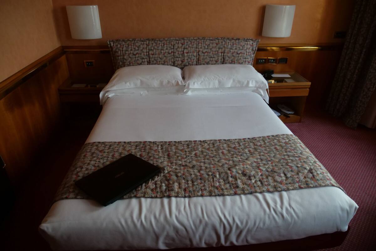 Una habitación de hotel con una cama bien hecha, una mesita de noche con lámpara y una pequeña cómoda.