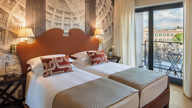 A double bed with a wooden headboard, two bedside tables with lamps, patterned wallpaper, and a balcony with a city view. - Starhotels Michelangelo (Rome)