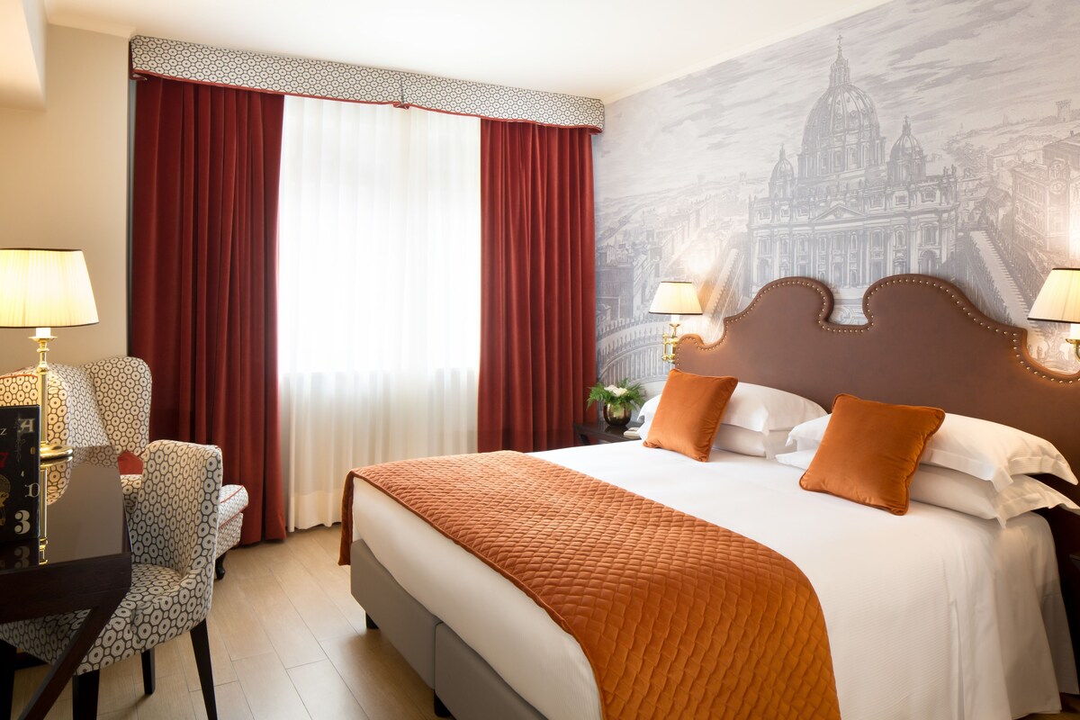 A hotel room with a bed, two bedside lamps, a chair, a desk, and a large window with curtains.