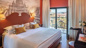 A hotel room with a large bed, a desk with a chair, a balcony with a table and chairs, and a mural of a famous building on the wall. - Starhotels Michelangelo (Rome)