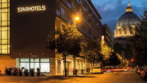 A StarHotels building with a large illuminated sign, parked motorcycles, and a historic dome in the background.