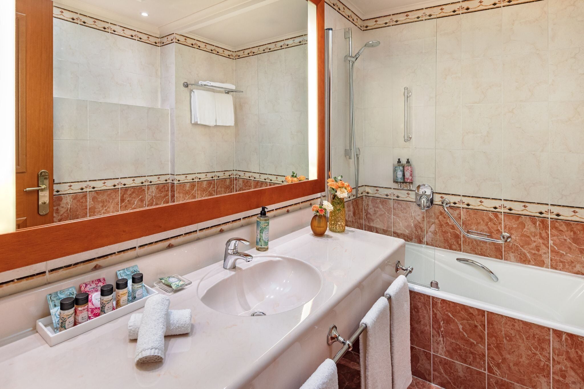 A bathroom with a large mirror, a sink with toiletries, a shower, and a bathtub.