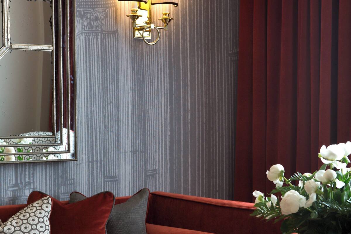 A red sofa with patterned pillows, a mirror, and wall-mounted lamps.