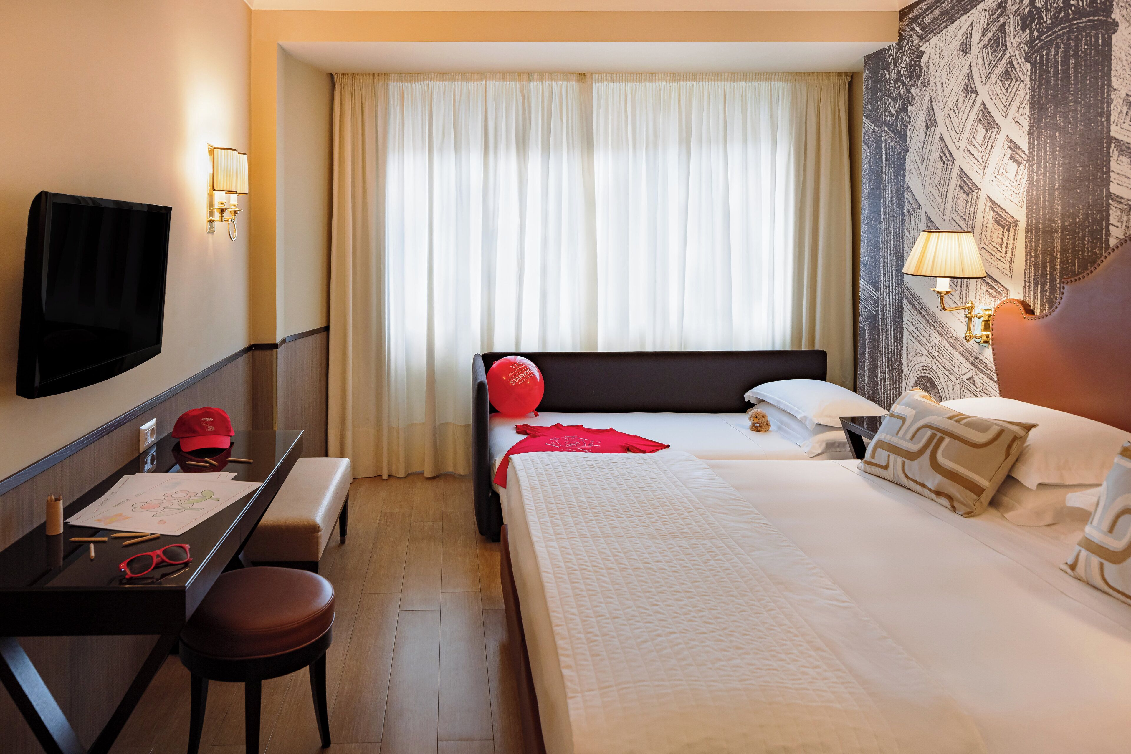A hotel room with a bed, a desk with a chair, a TV, and a window with curtains.