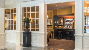 A lobby with a marble floor, a bar area with stools, and a large window with a plant in the center.