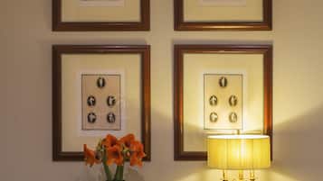 A wall with four framed pictures, a table with a lamp, and a vase with flowers.