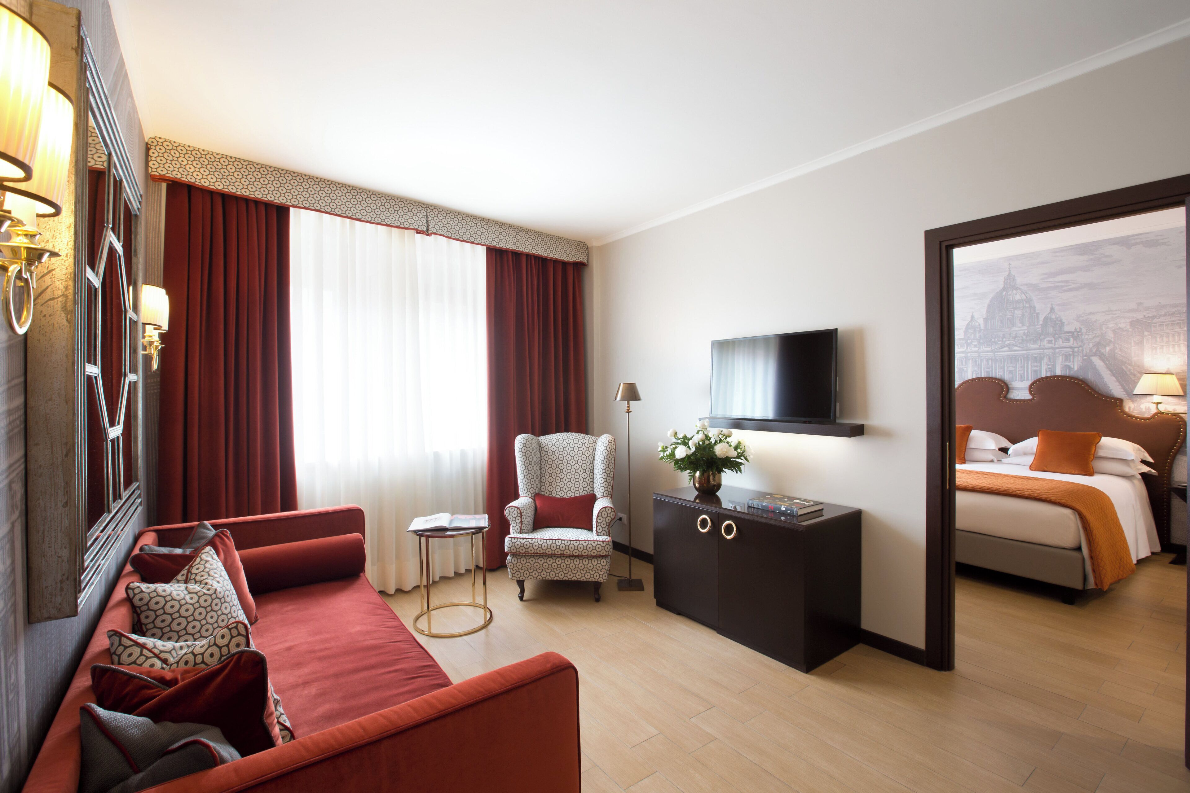 A hotel room with a sofa, armchair, TV, and a bed.