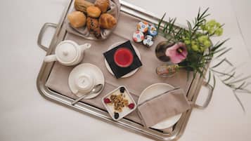 A tray with croissants, a teapot, a cup of tea, a bowl of granola with berries, and a small vase with flowers.