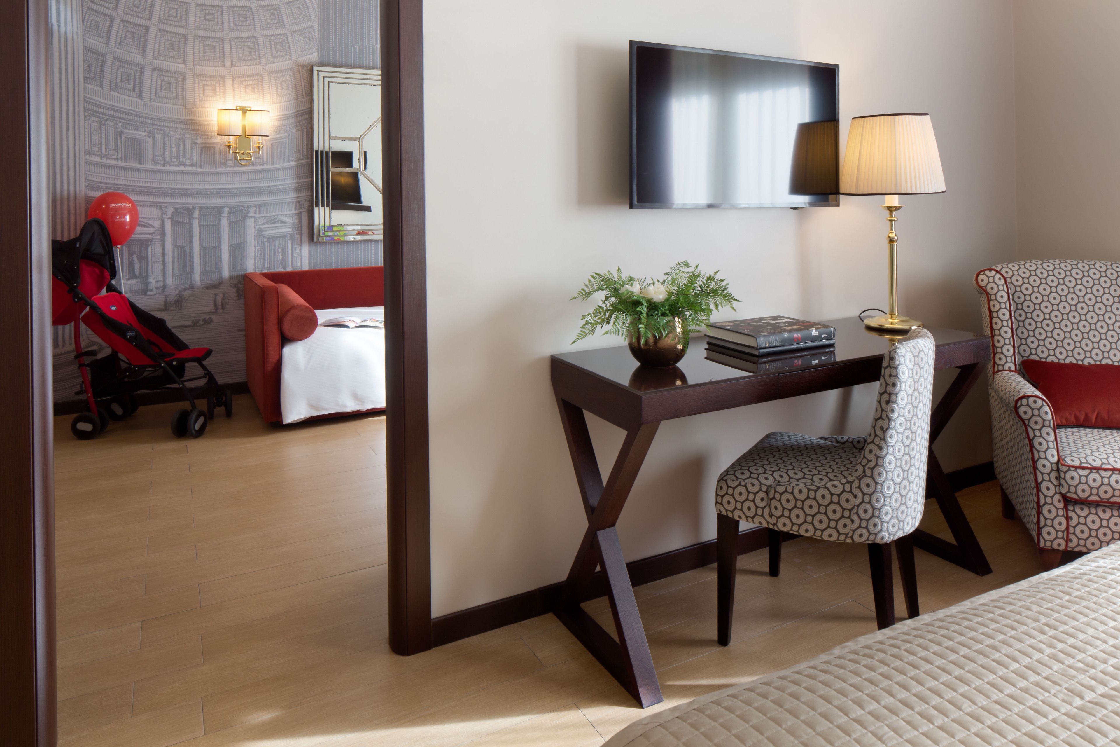 Een hotelkamer met een bed, een bureau met stoel, een televisie, een lamp en een klein tafeltje met een plant.