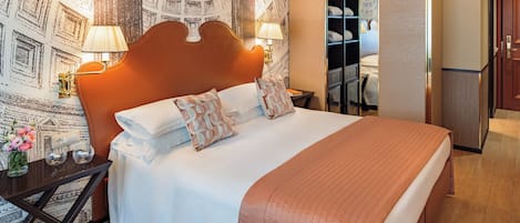 A neatly arranged hotel room with a large bed, bedside lamps, a small table with a vase of flowers, and a wardrobe.