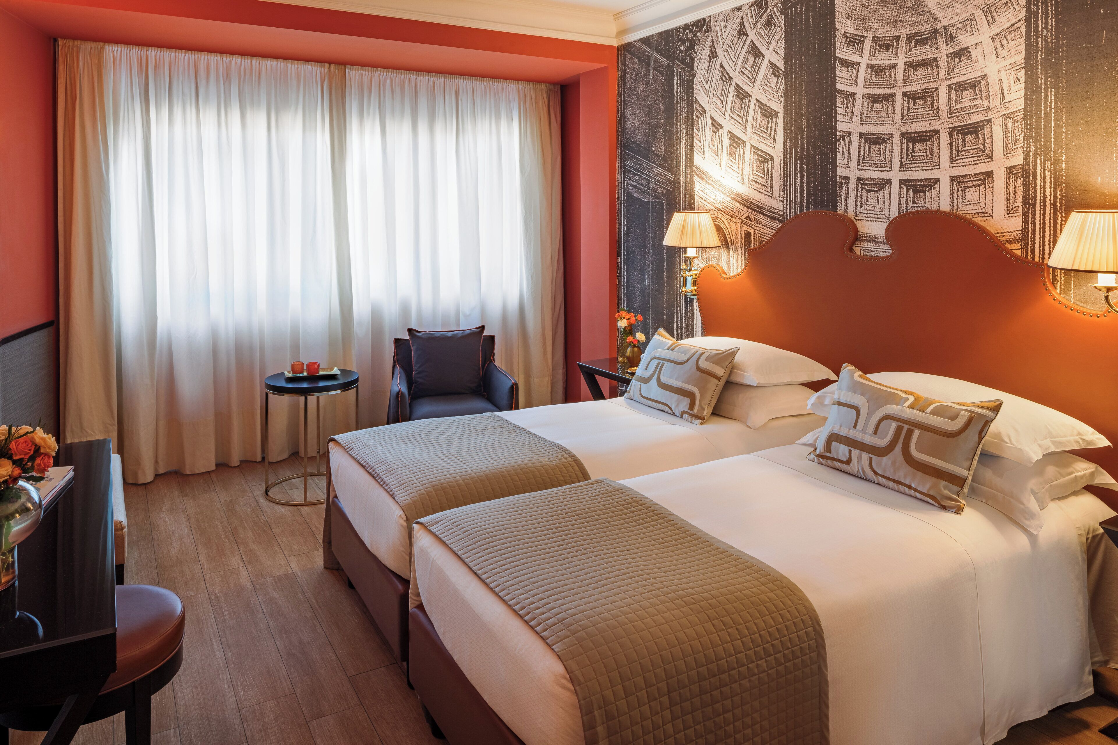 A hotel room with two beds, a desk, a chair, a small table, and a large window with curtains.