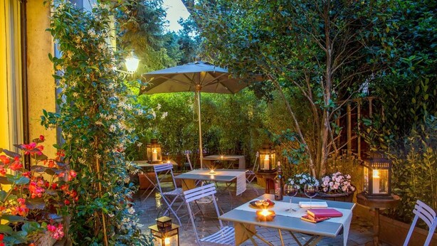 An outdoor patio area with tables and chairs, surrounded by lush greenery and flowering plants. - Hotel Panama Garden (Rome)