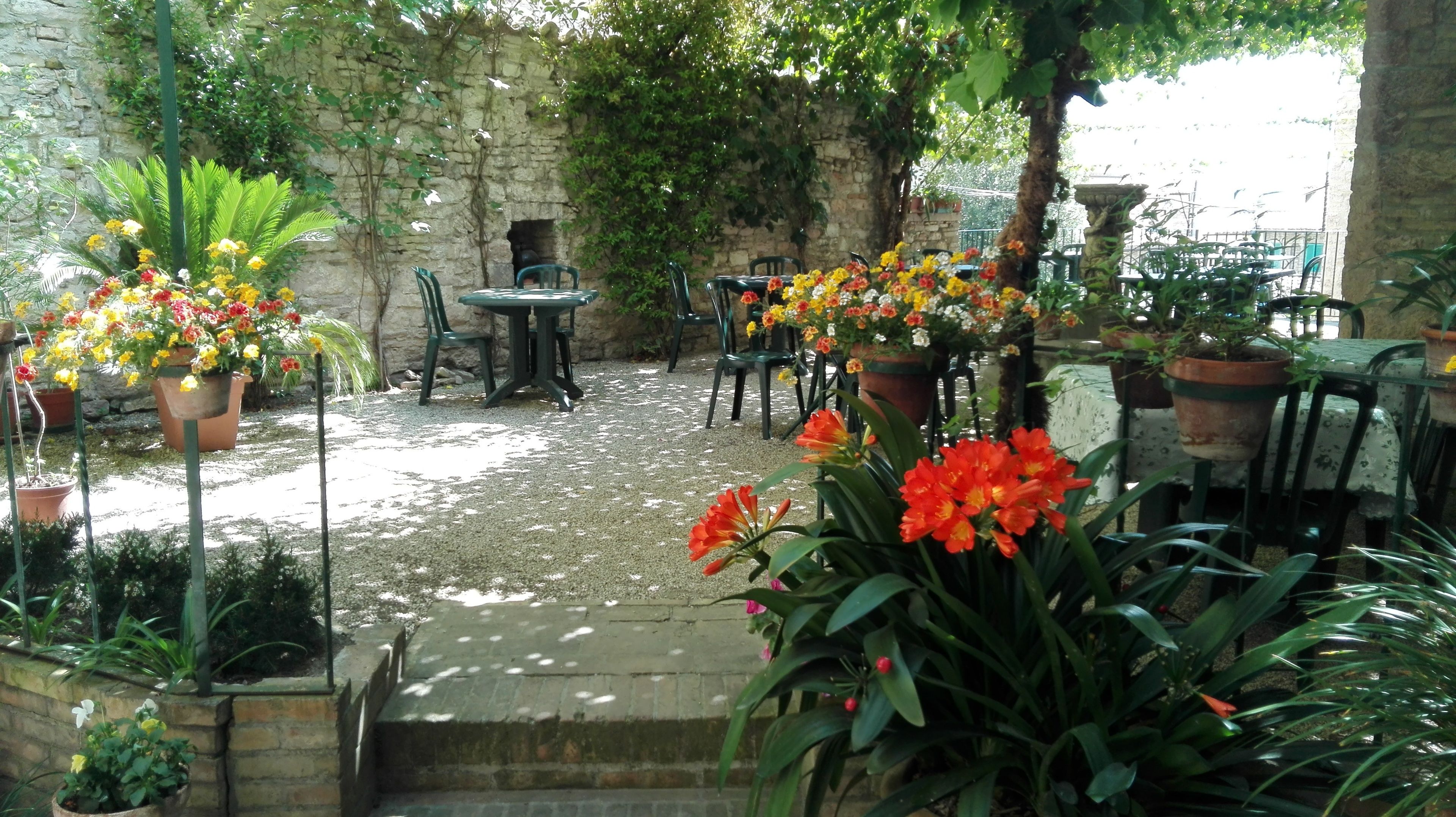 Patio esterno con pareti in pietra, piante in vaso e posti a sedere.