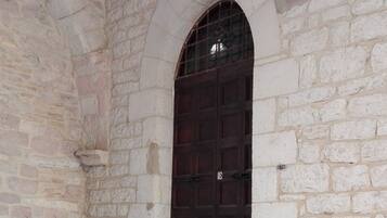 A stone building with a dark wooden door, a small arched window, and a set of stone steps leading up to the door.