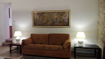 A living room with a sofa, two side tables with lamps, a framed painting on the wall, and a staircase in the background.