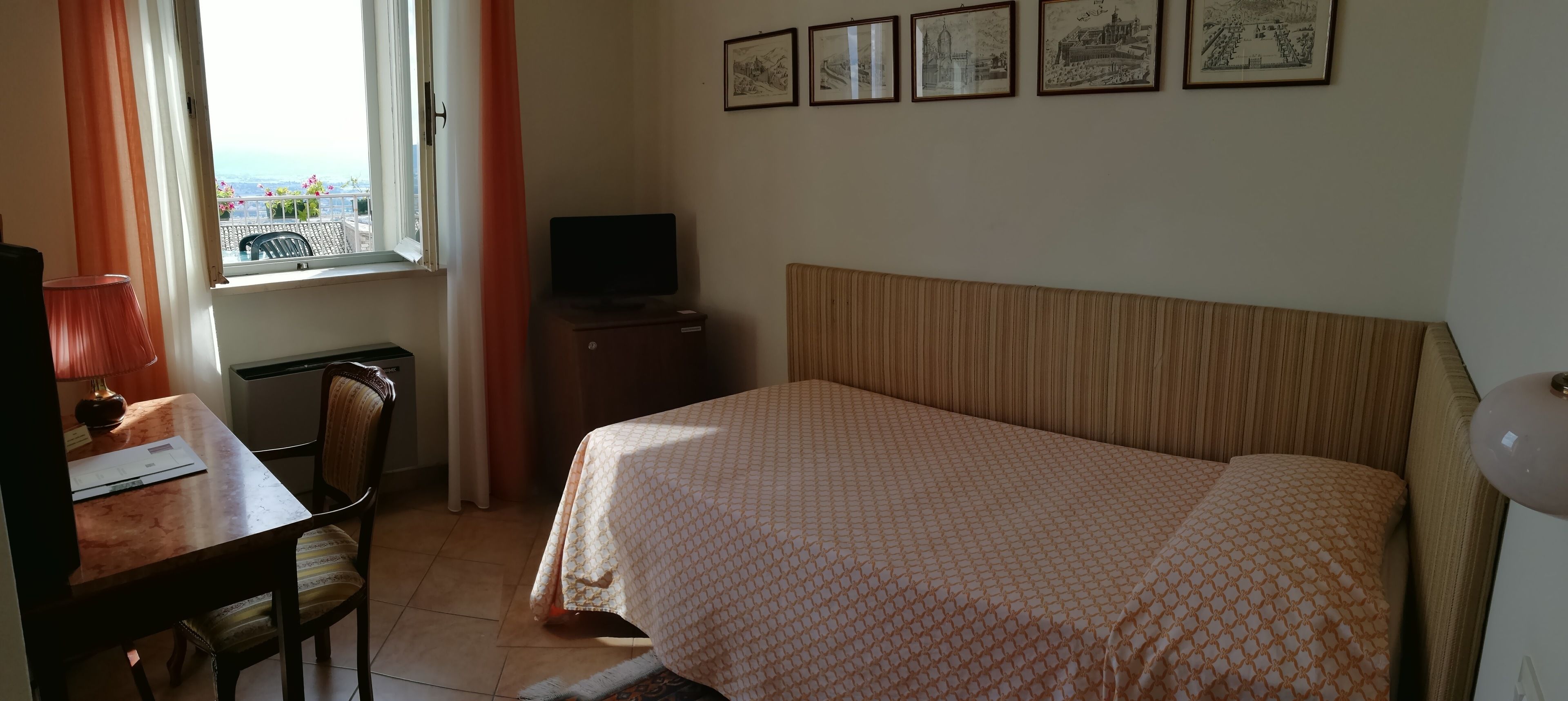 Habitación de hotel con cama, escritorio con lámpara, televisión y cuadros en la pared.