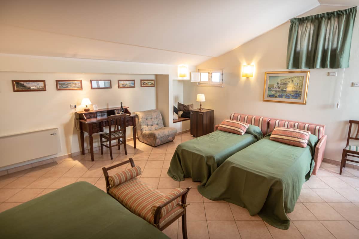 A hotel room with two beds, a desk, a chair, and a small sofa.