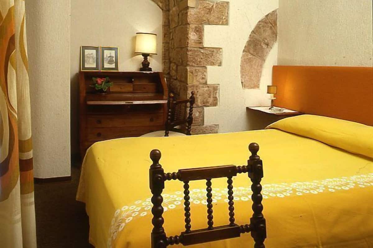 A room with a bed, a desk, and a stone archway.