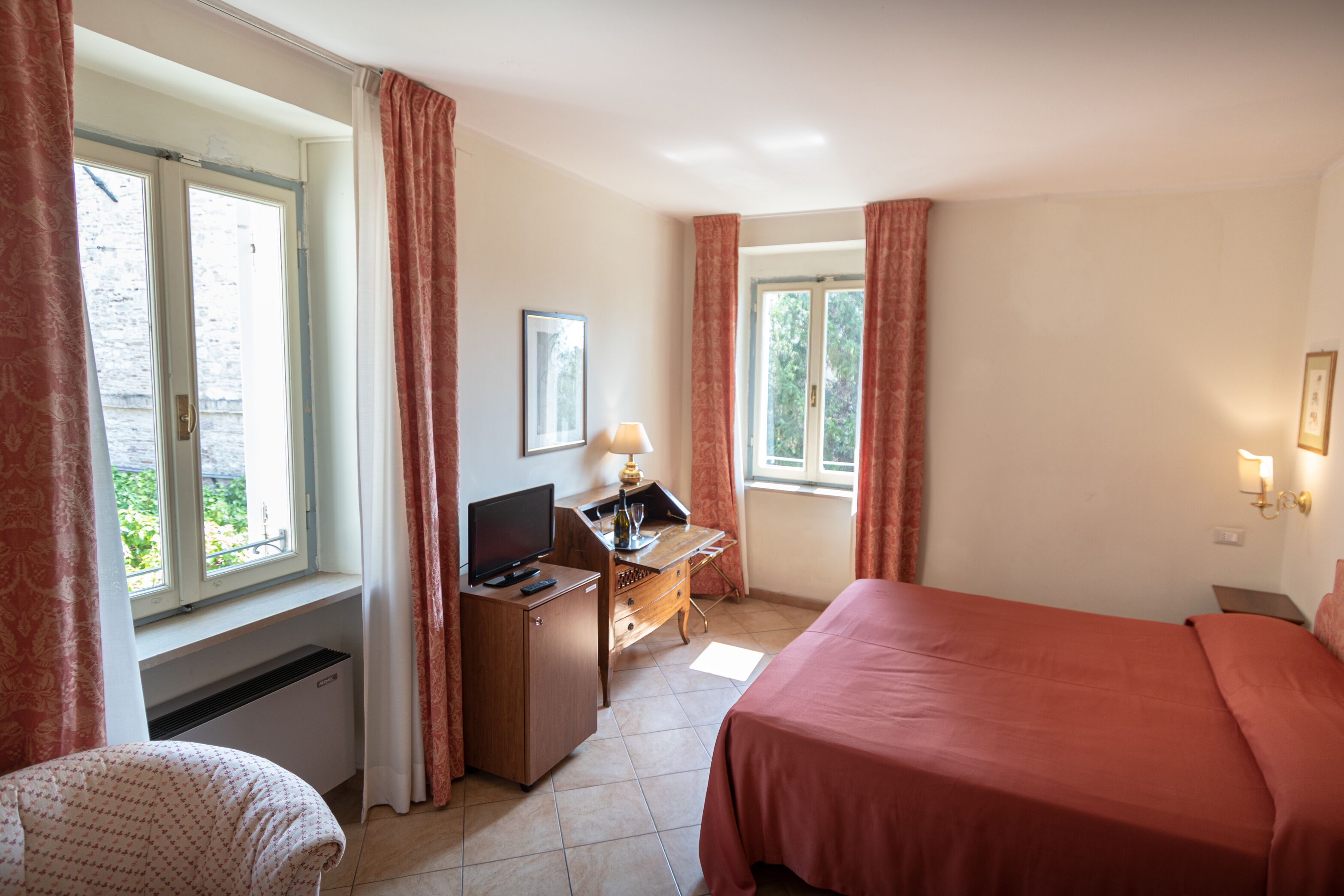 Una camera d'hotel con un letto, una scrivania con un computer, una sedia e una finestra con tende.