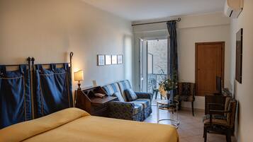A hotel room with a bed, a sofa, a small table with a lamp, a TV, and a balcony with a view.