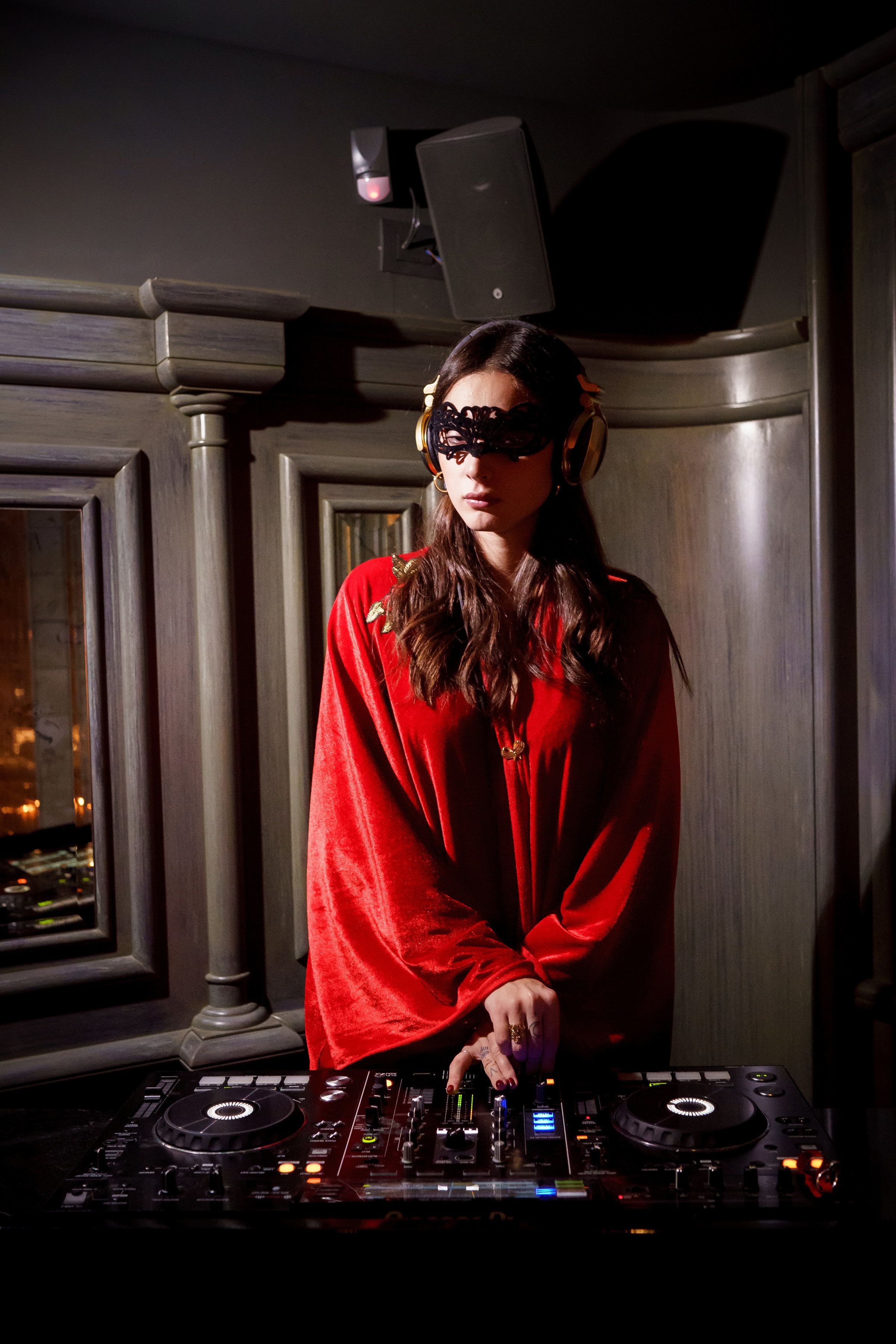 Una persona con bata roja de pie detrás de una consola de DJ en una sala con paneles de madera.