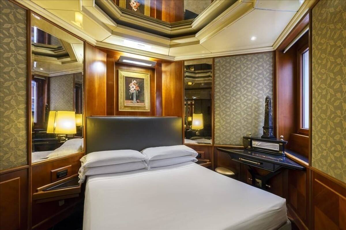 Une chambre d’hôtel avec un grand lit, un bureau avec une lampe, un miroir et un tableau au mur.