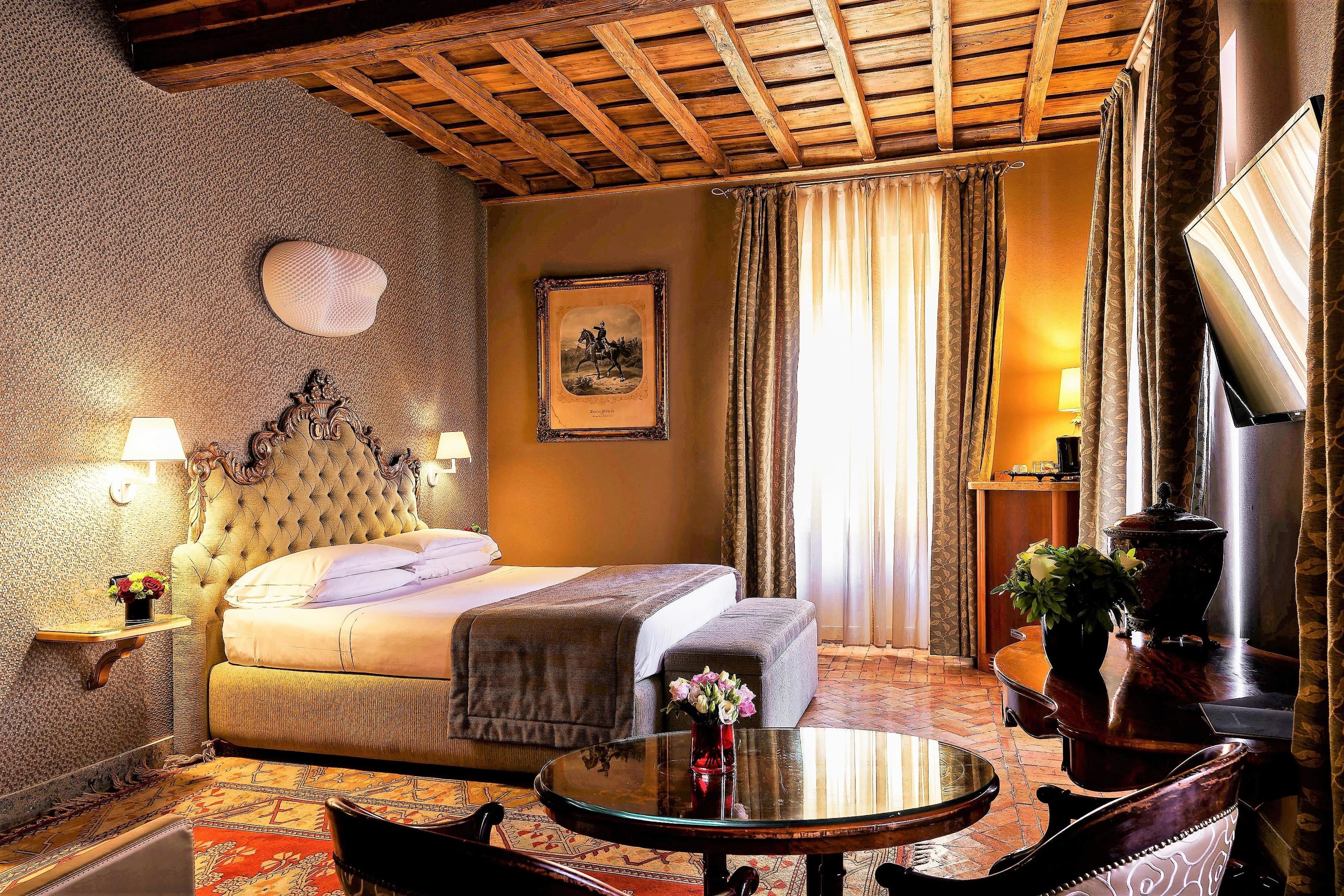 A hotel room with a large bed, a sitting area with a table, a TV, and a framed picture on the wall.
